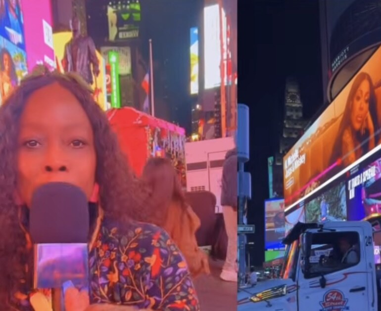 Mona reporting in Times Square with K. Michelle's Jesus and Whiskey billboard behind her